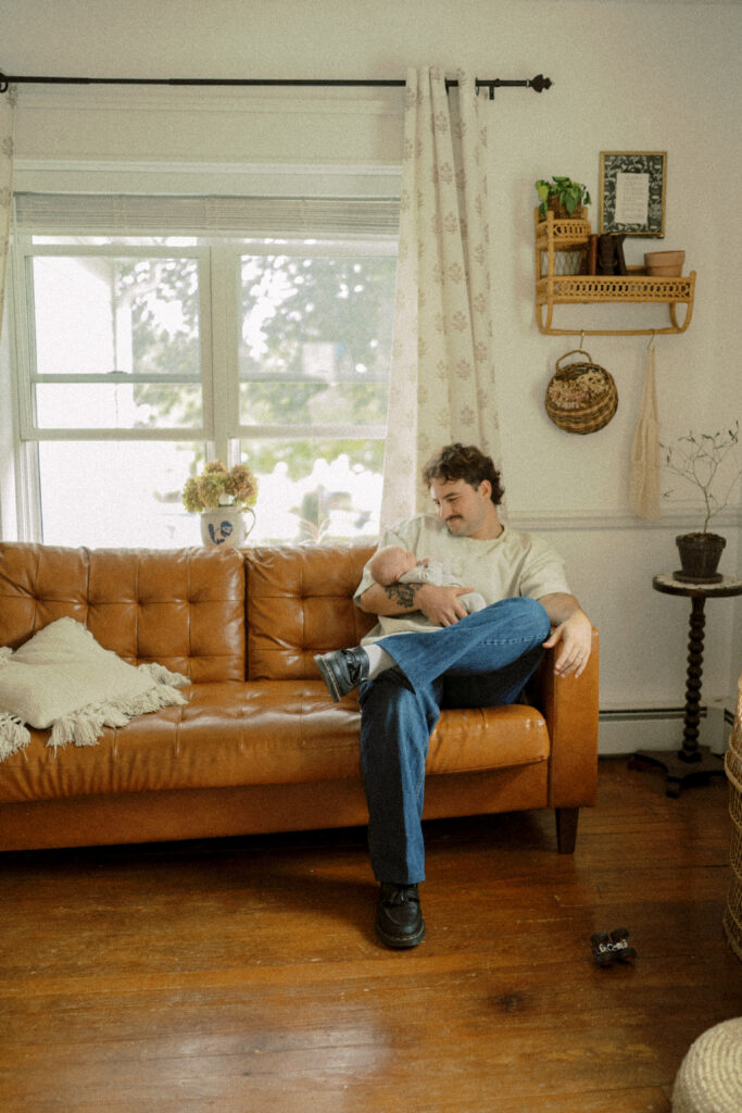 main line newborn photographer - Jessica Mae - captures a dad on his couch while he's looking down at his newborn son