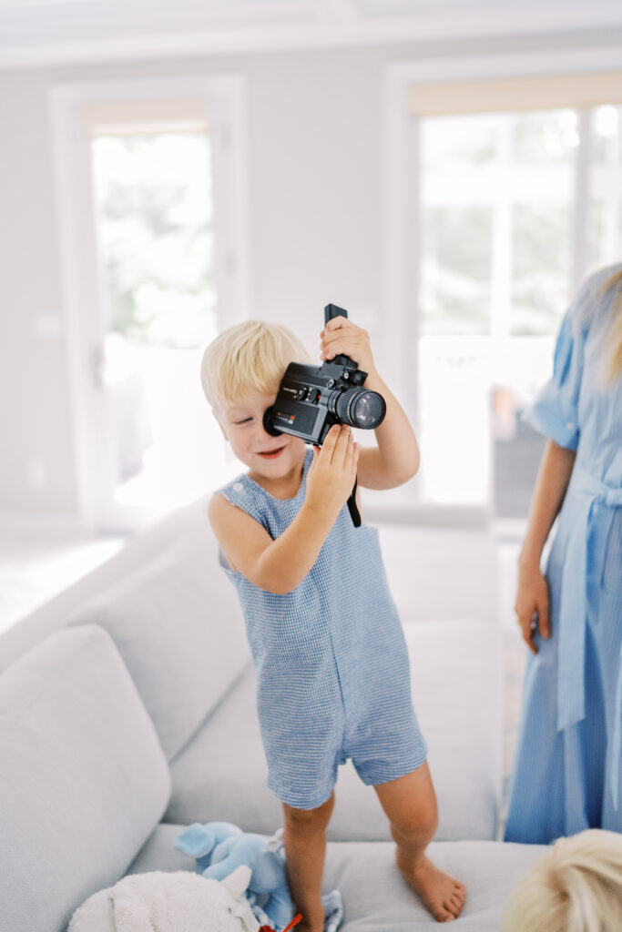 blond toddler boy plays with super 8 camera during a fun in home family photos with toddlers session