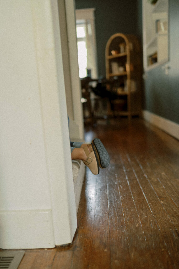 little boy plays hid and seek on the stairs. only his shoes are visible as they peek out from the stair way during his family photoshoot at home