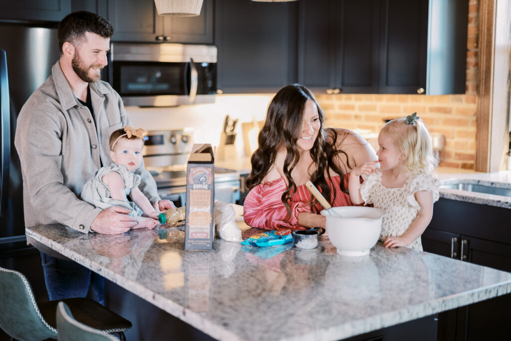 mom and dad interact with their two small daughters while they make pancakes in their kitchen