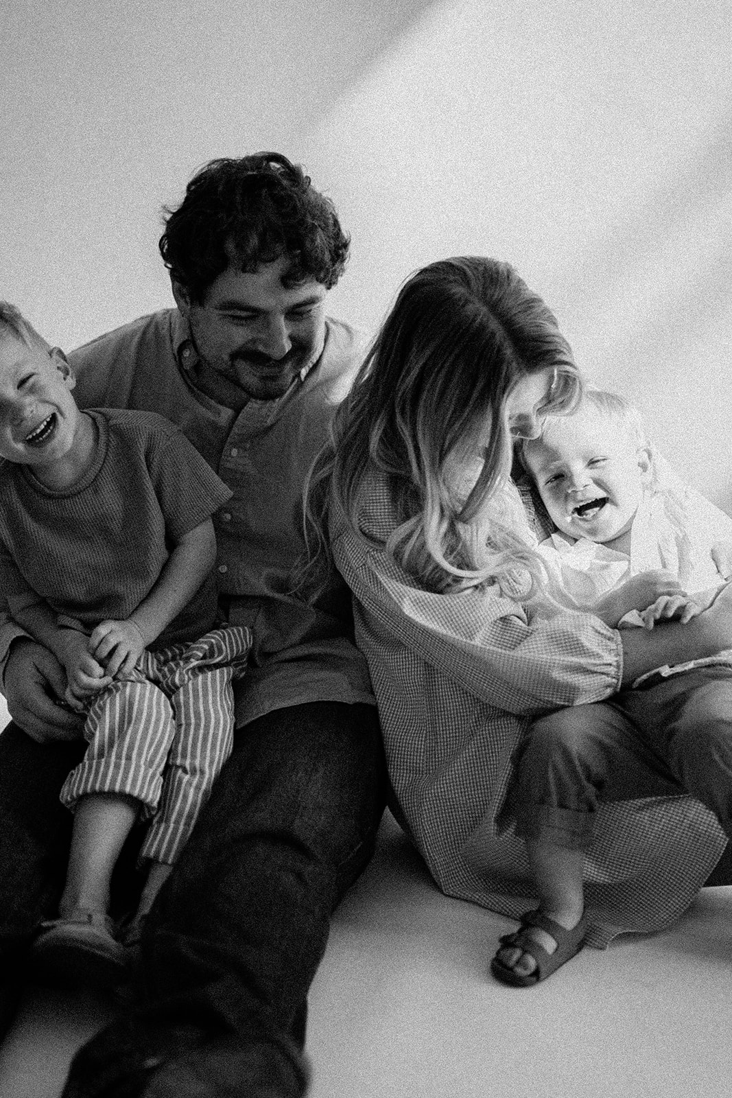 a family of a mom, dad and two little boys. the boys' are on mom and dad's lap and they are giggling