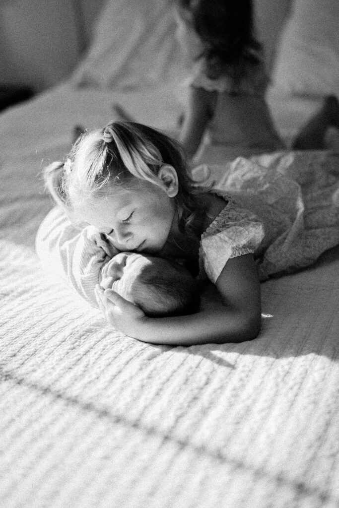 A little girl cuddles her newborn baby brother on their parents bed. They are having fun during their Lancaster Newborn Photography Session.