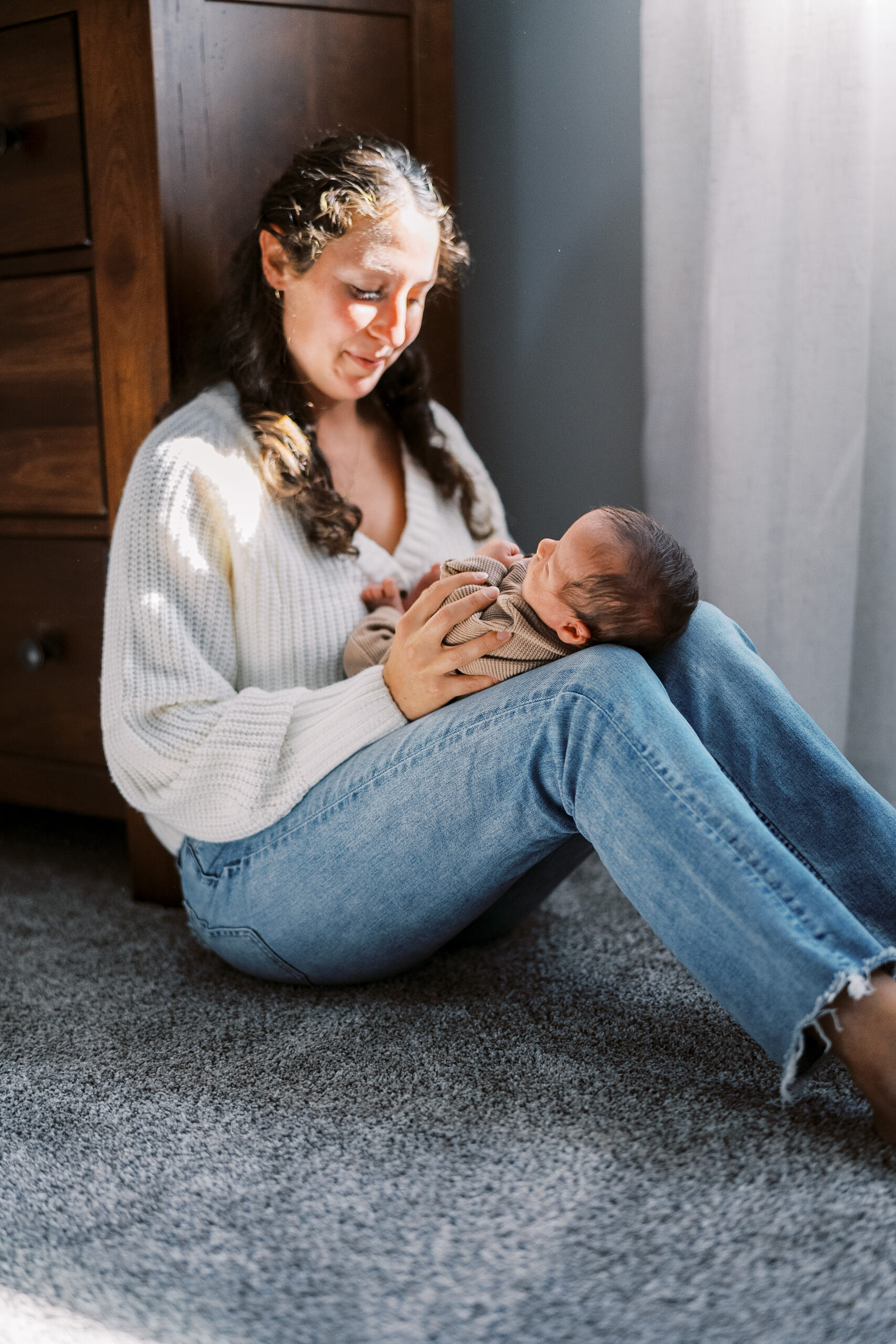 Mom sits on the floor of her bedroom, cuddling with her newborn baby during her Harrisburg Newborn Photography session.